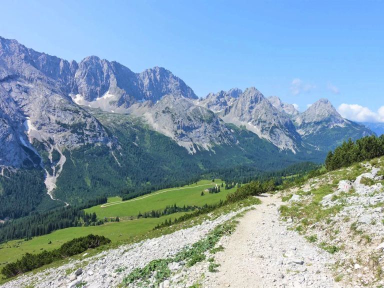 Steiniger Wanderweg mit Almwiesen und Bergen im Hintergrund nahe der Ehrwalder Alm in Österreich.